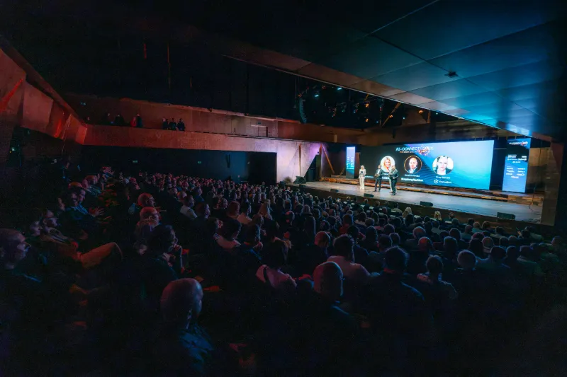 Pełna widownia sali koncertowej Filharmonii w Szczecinie podczas otwarcia AI-CONNECT 2026; na scenie prowadzący, na ekranie przedstawiciele organizatorów: Klastra IT, Kongsberg Maritime i Enovation