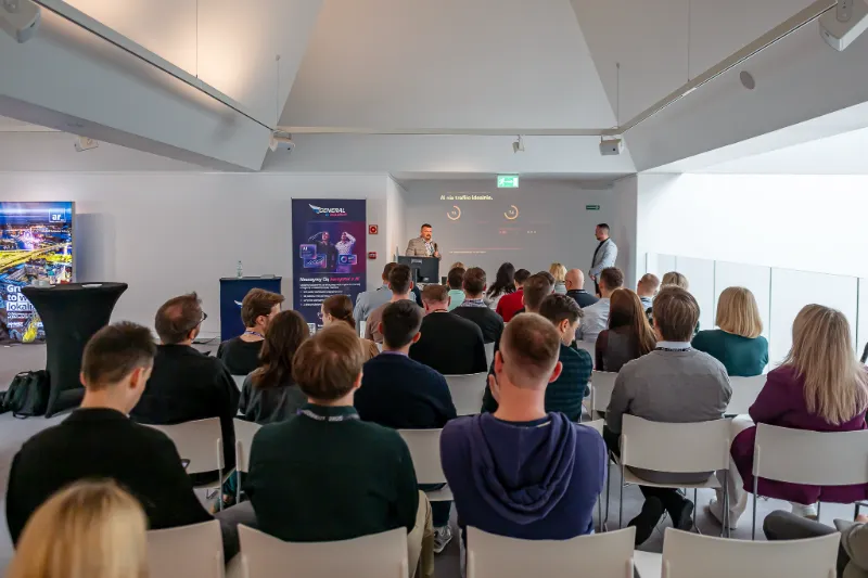 Pełna sala warsztatowa widziana od tyłu; prowadzący przy ekranie z wynikami testu Lighthouse, obok roll-up General AI Academy